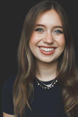 Headshot of a smiling young blonde woman with blue eyes wearing a black top and layered necklaces.