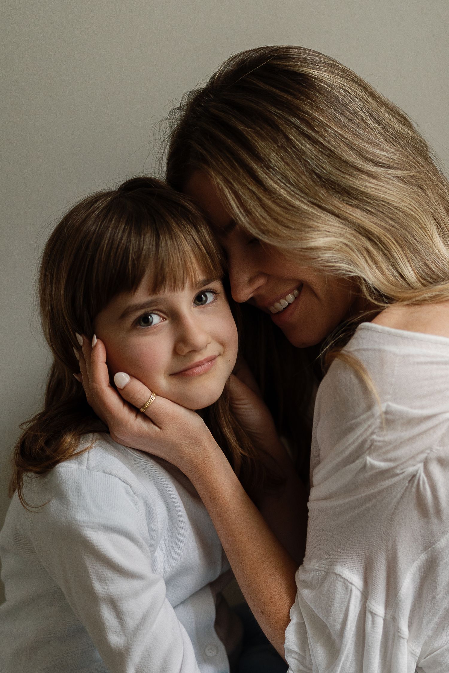 Loving mother smiles while gently cradling daughters face in tender indoor portrait.