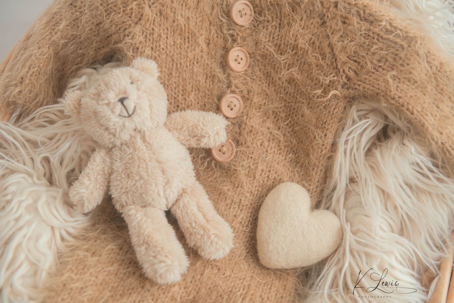 Soft beige knit newborn outfit with teddy bear and heart prop on fluffy white fur backdrop for newborn photography.