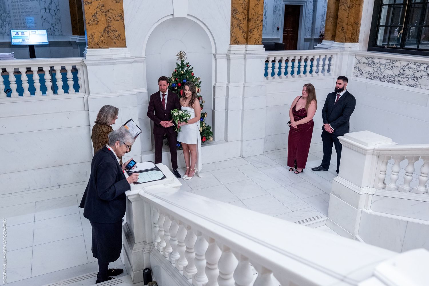 A bride and groom stand together in a grand, ornate hall during their wedding ceremony.