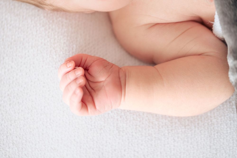 Close-up of a newborn baby's tiny hand and chubby arm resting on a soft white blanket.