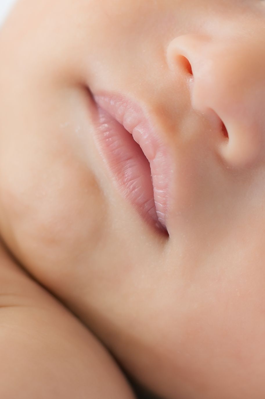 Close-up macro photo of a sleeping baby's soft pink lips and nose, showcasing delicate infant facial features.