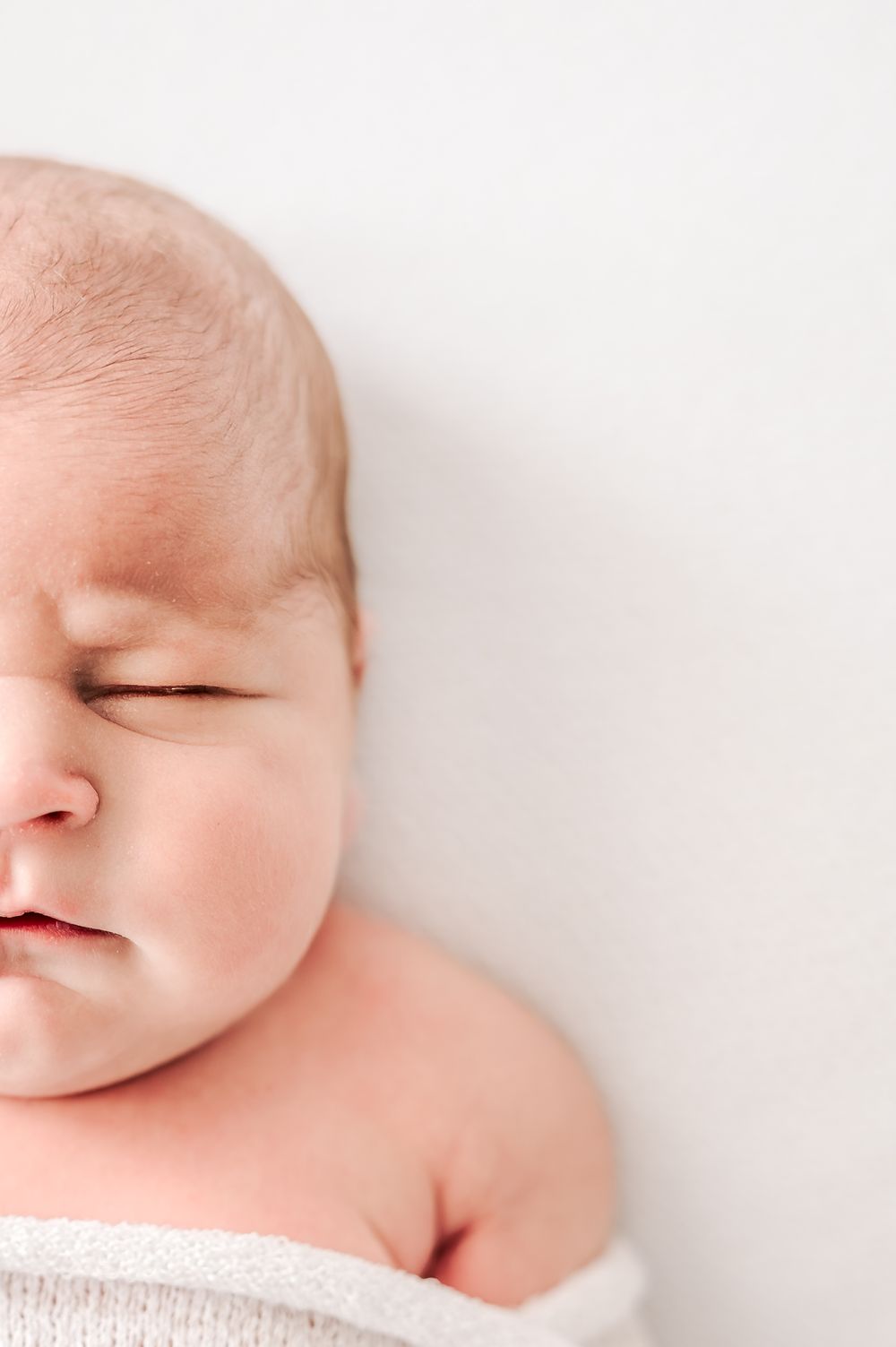 Close-up portrait of a peaceful sleeping newborn baby wrapped in a soft white blanket.