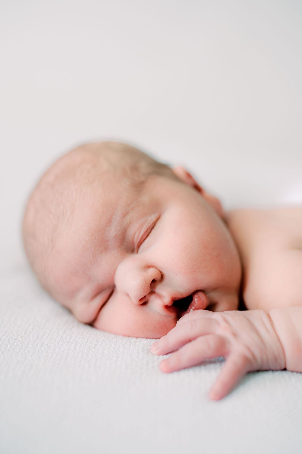 Peaceful sleeping newborn baby with tiny hand near face resting on white blanket.
