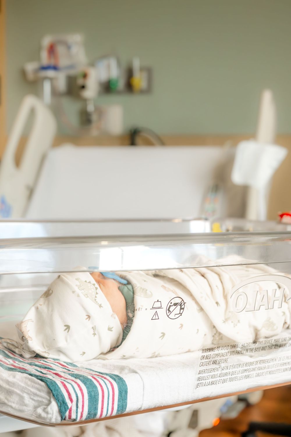 Newborn baby swaddled in white blanket sleeping peacefully in a hospital bassinet after birth.