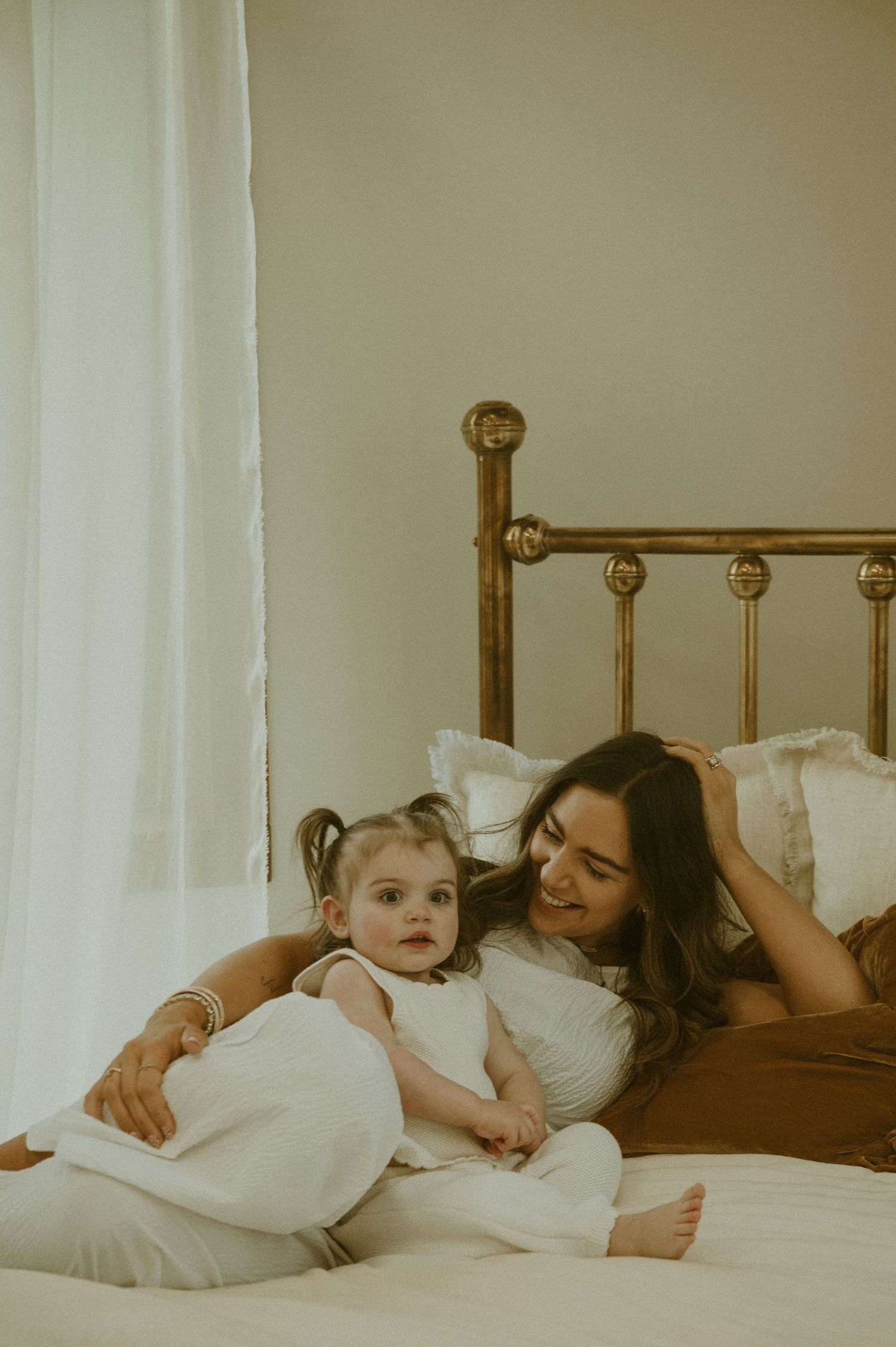 Two people share a tender moment while resting together in bed with white linens and pillows.