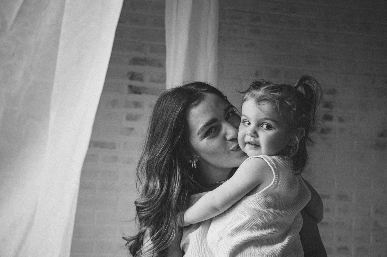 A series of black and white photographs showing tender moments between a parent and child in front of a brick wall.