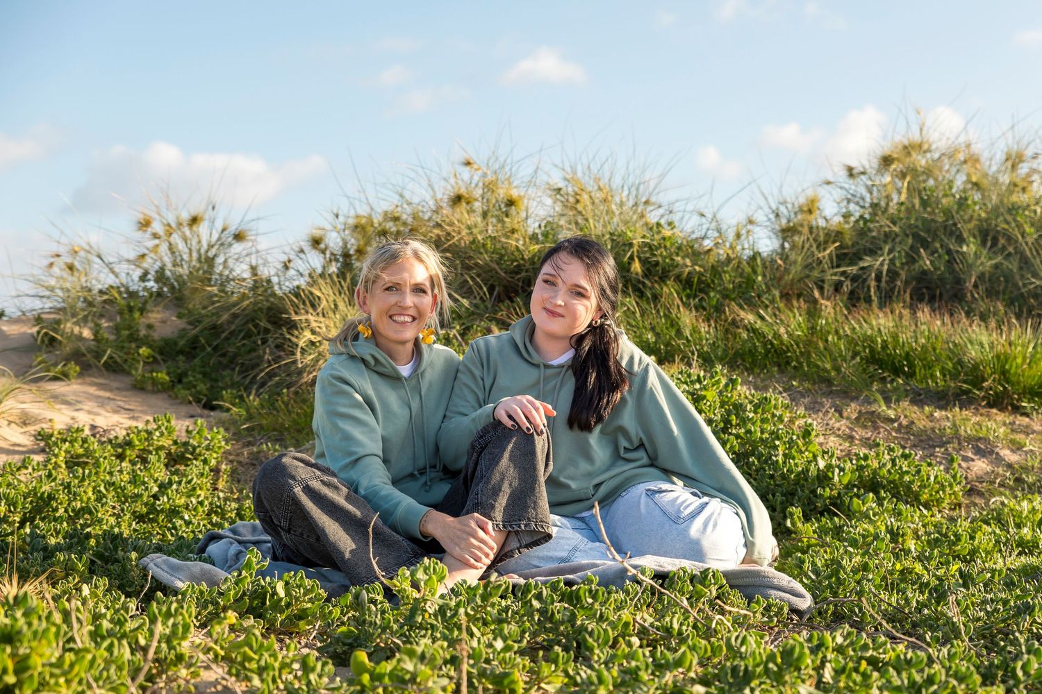 Candid moment of a mother and daughter smiling together on the dunes with soft green bushland behind them