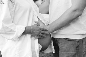 A couple in casual attire holds hands tenderly in a black and white photograph.
