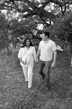 A couple takes a romantic stroll together under large oak trees in a black and white photograph.