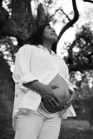 Black and white maternity photo series showing a pregnant woman in white dress cradling her belly outdoors.