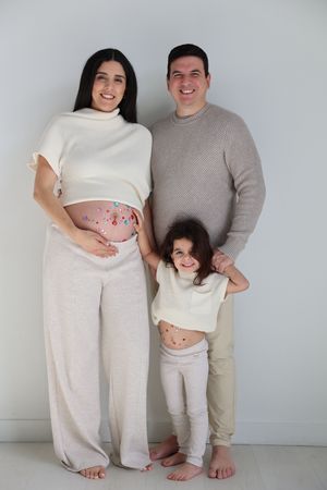 A series of maternity photos showing a couple in white outfits with playful heart decorations on a pregnant belly.