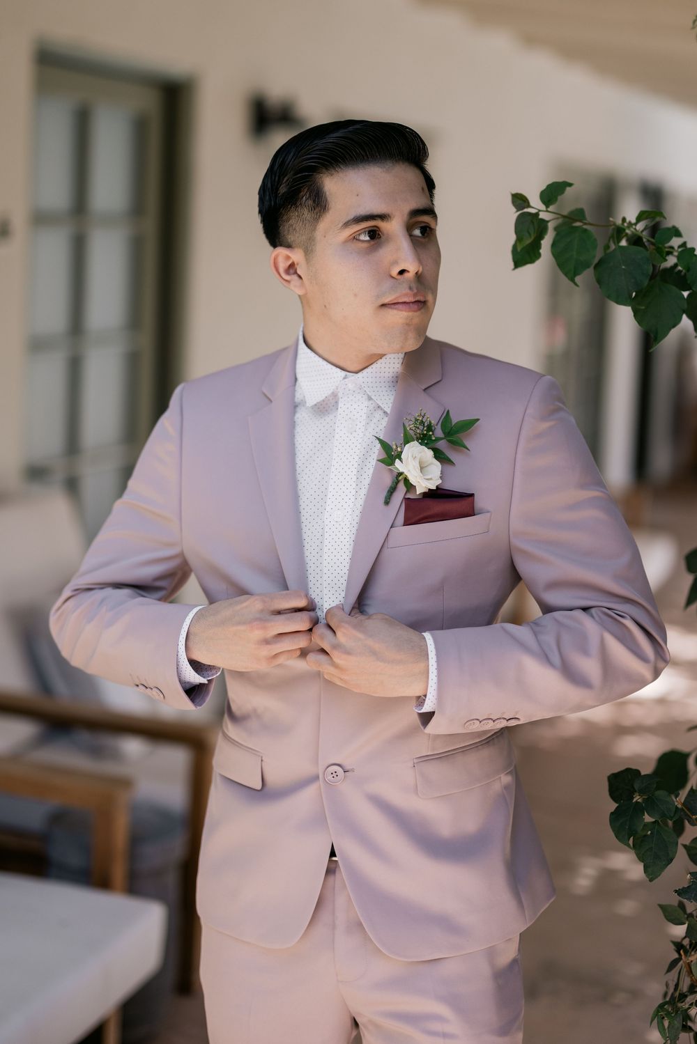 Handsome groom in a blush pink suit with boutonniere adjusting his jacket before the wedding ceremony.