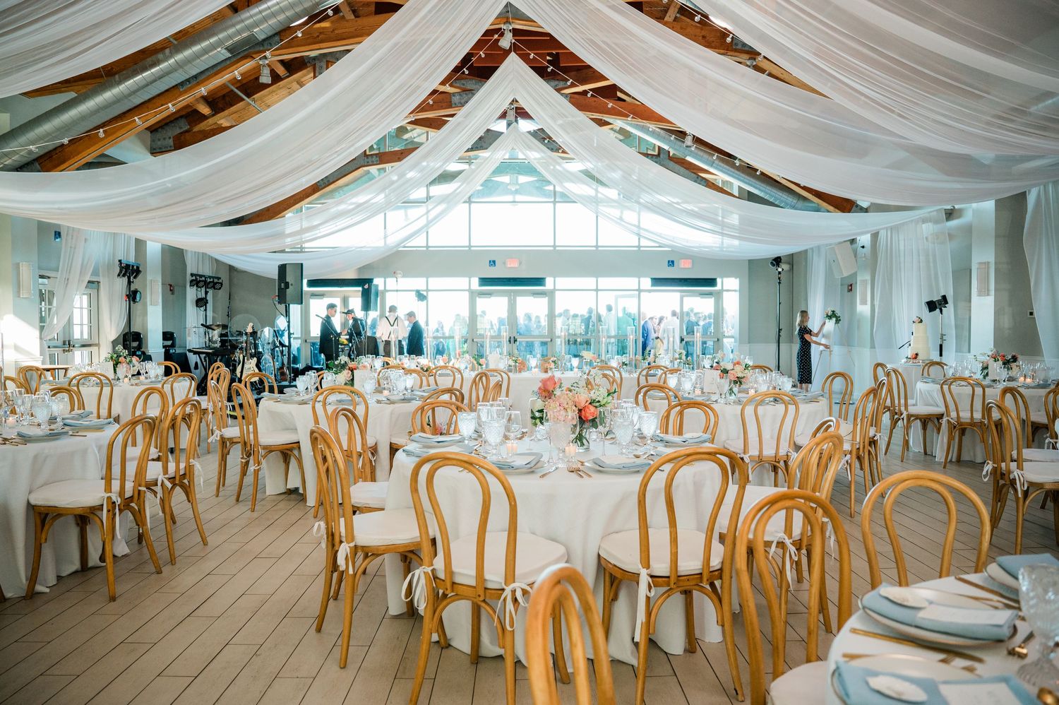 Elegant wedding reception venue with white draped ceilings, wooden chairs, and round tables set for a celebration.