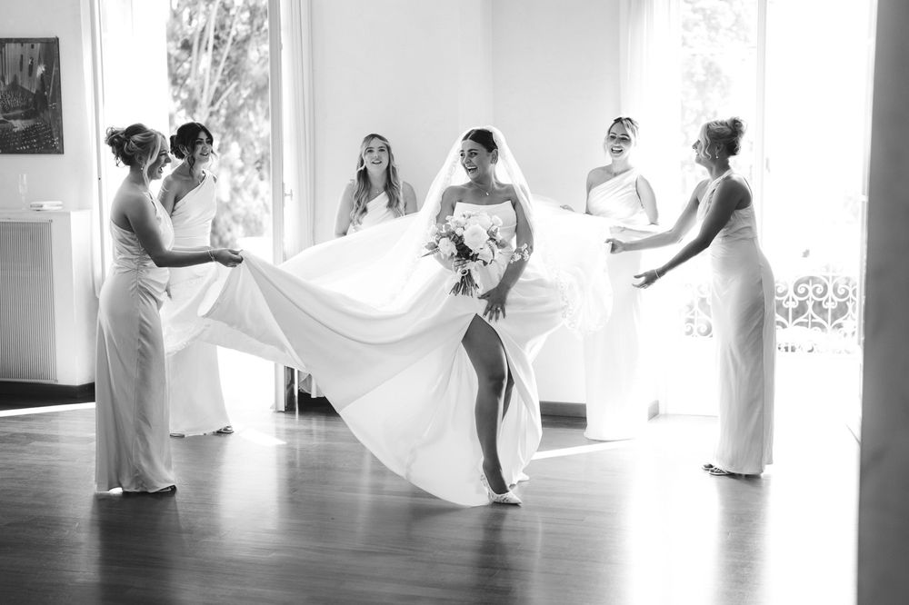 Bridesmaids adjust the bride's dress during wedding preparations in Sanremo.