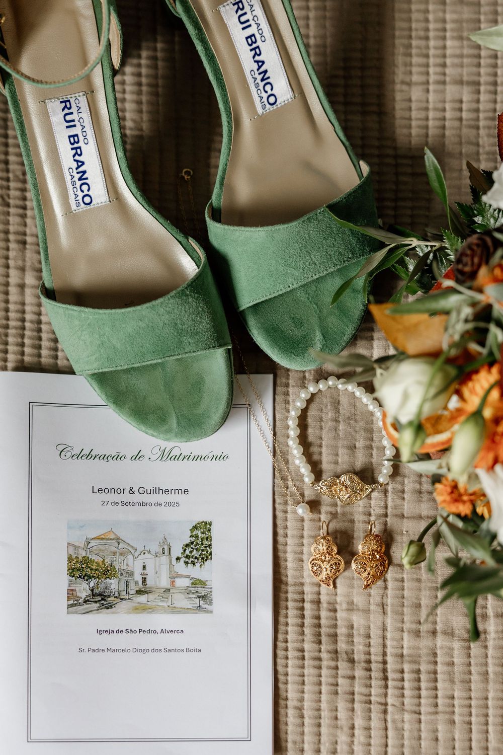 A pair of green suede high heels and a wedding invitation on a woven mat.