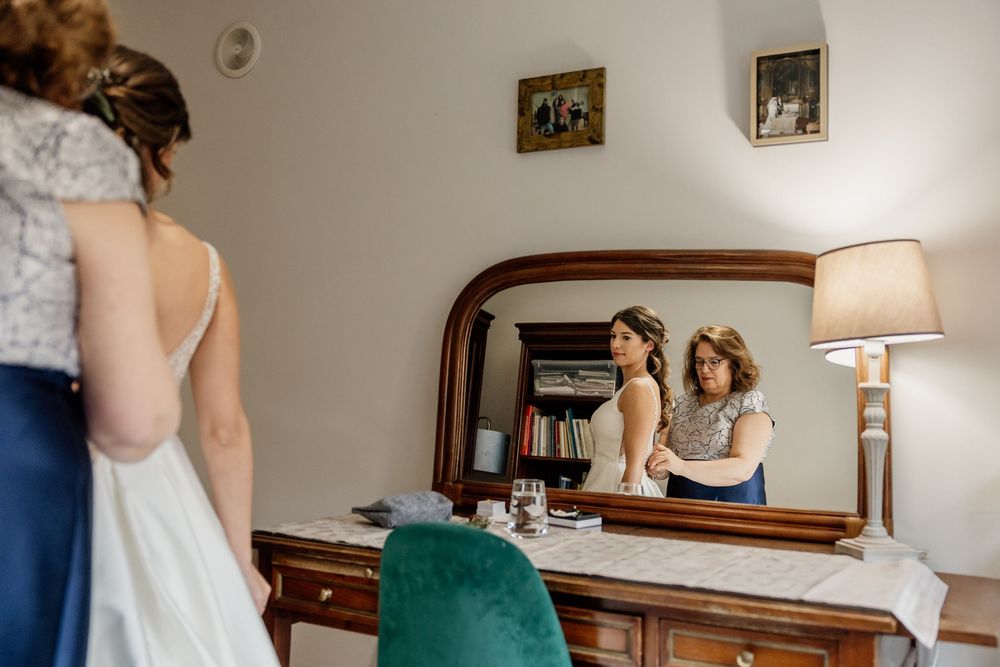 A woman stands in front of a mirror, wearing a white dress and looking at her reflection.