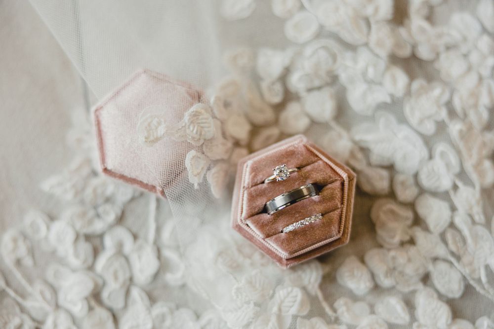 Wedding rings rest in hexagonal rose gold ring boxes surrounded by delicate white floral details.