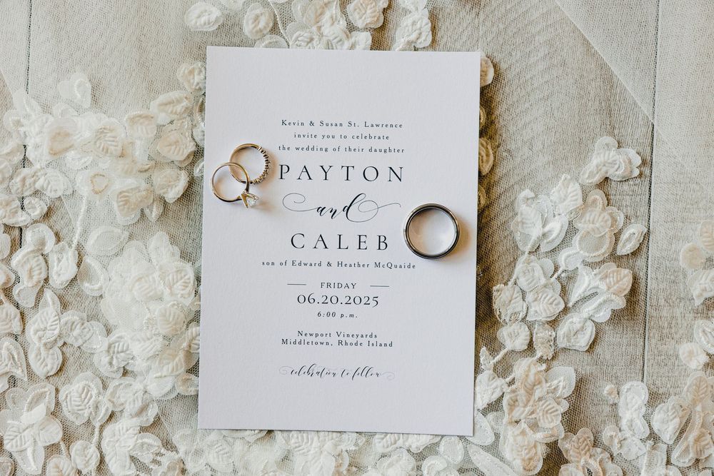 Elegant white wedding invitation with gold rings displayed on a textured floral background.