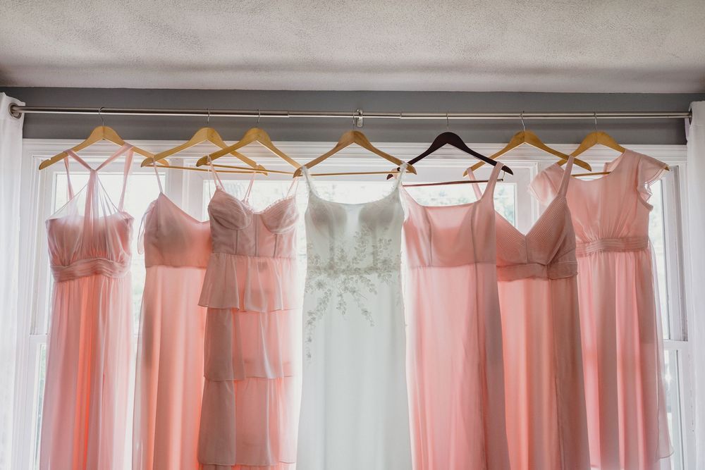 Pink bridesmaid dresses hanging on wooden hangers against a light gray wall.
