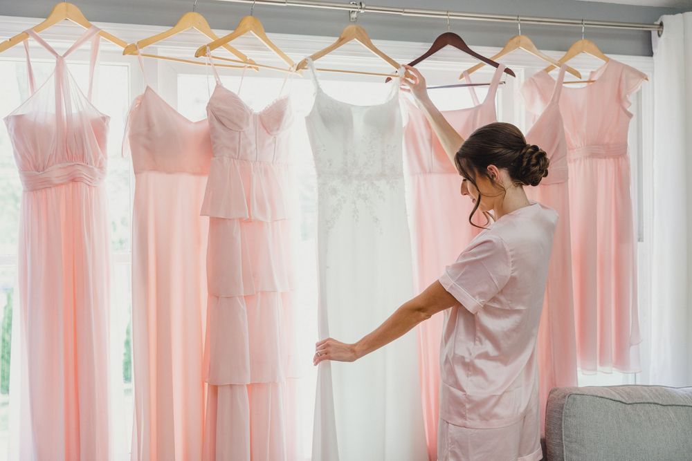 Row of blush colored dresses displayed on wooden hangers in a bridal preparation room.