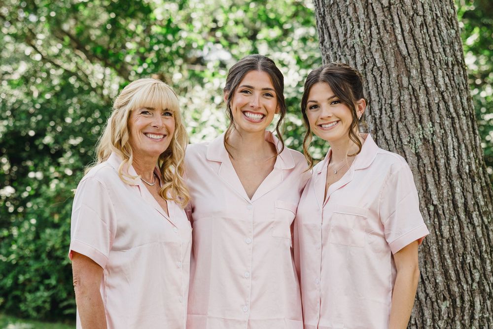 A group wearing matching pink button-up shirts poses together outdoors against a tree backdrop.
