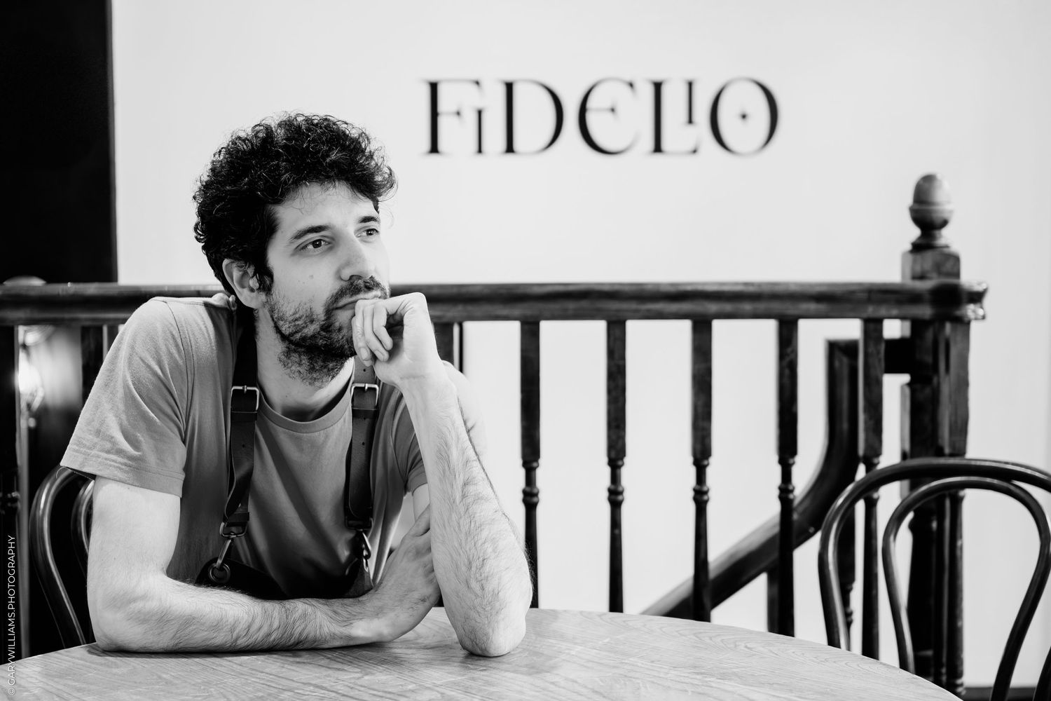 Black and white portrait of a person with curly hair sitting at a table under a Fidelio sign.