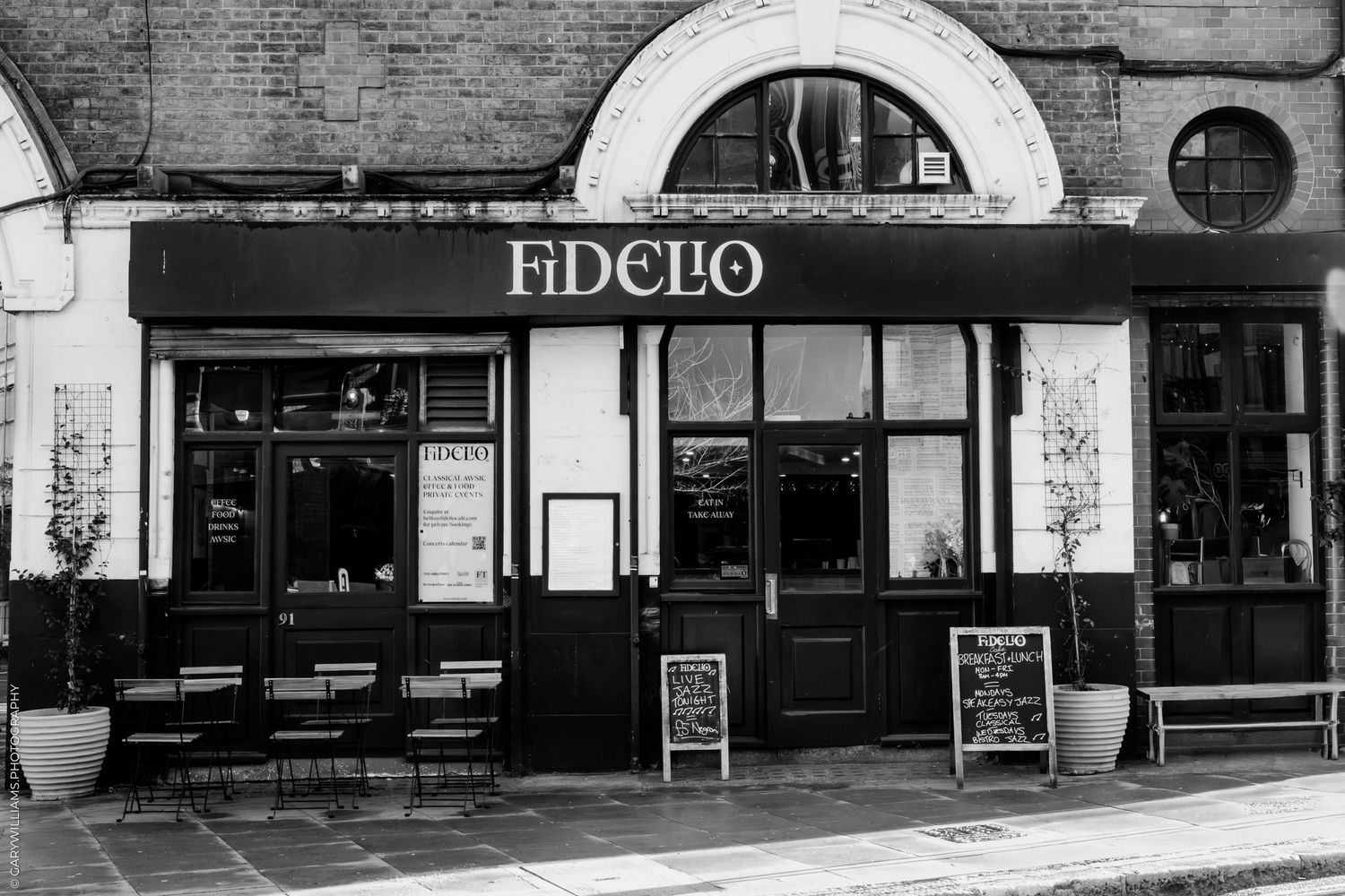 Black and white panoramic view of vintage storefronts and shops along a historic commercial street.