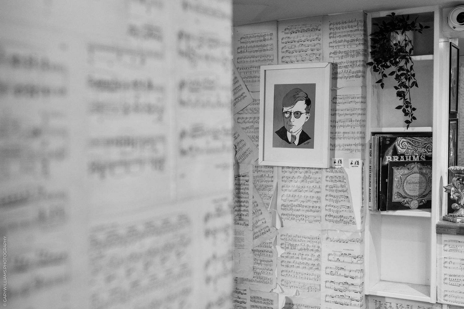 Black and white photograph showing newspaper clippings and photos mounted on a wall in a gallery or exhibit setting.