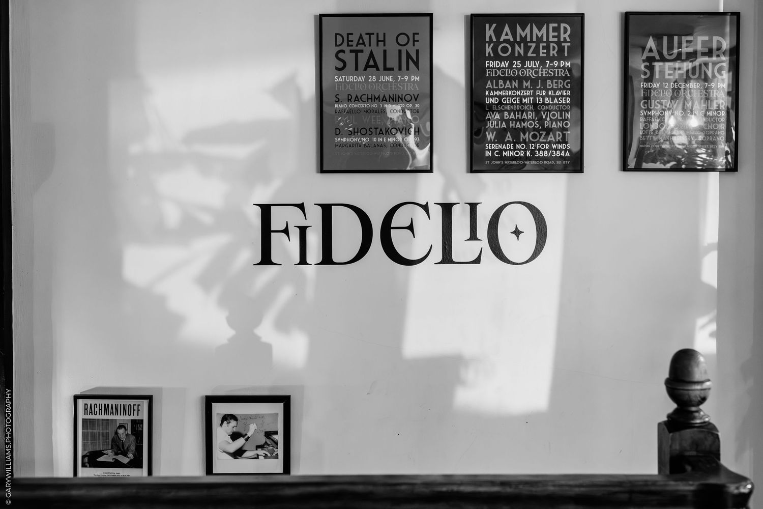 Black and white photograph showing Fidelio text on a wall with vintage posters and a small bust on display.