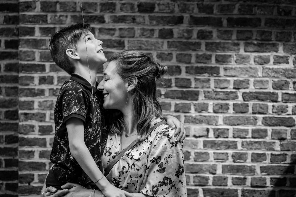 A joyful black and white portrait against a brick wall capturing a tender moment between parent and child.