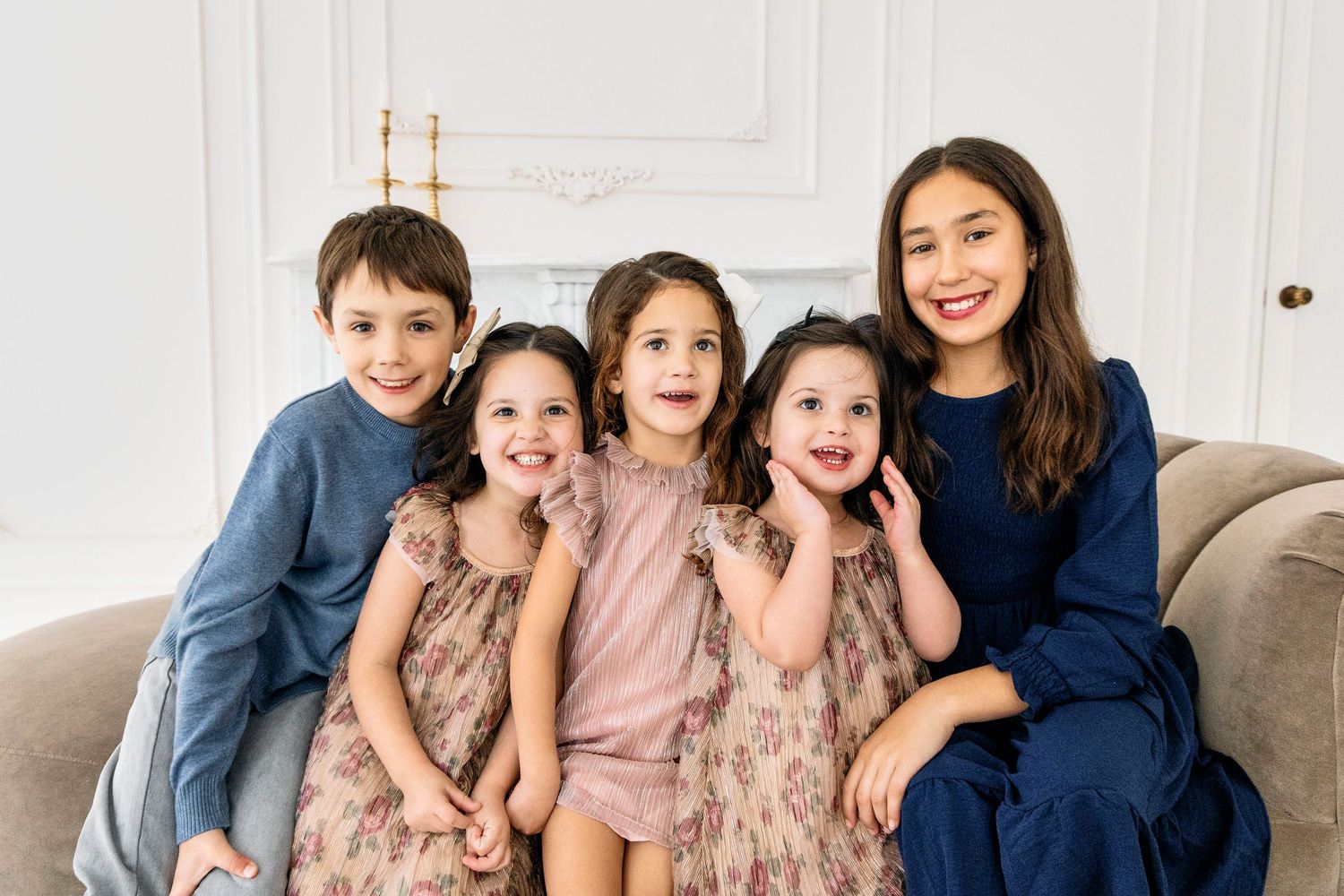 A group sits together on a light gray couch in a bright white room wearing coordinated blue and pink outfits.