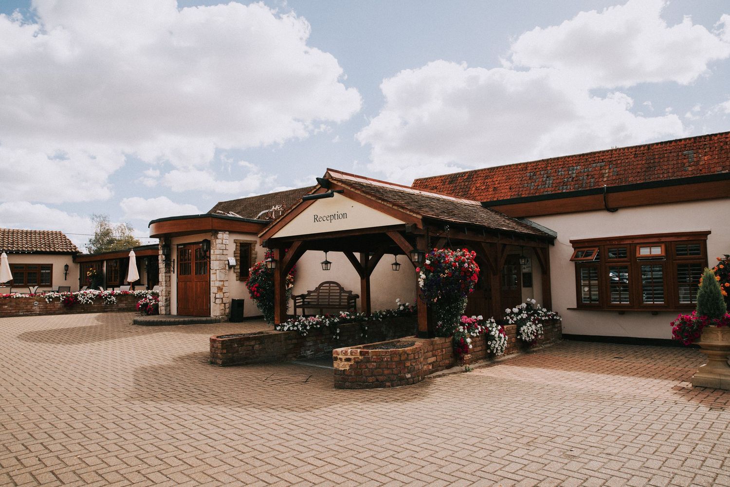 Ye Olde Plough House - countryside venue reception entrance with brick paving, floral displays, and wooden canopy under cloudy Essex skies.