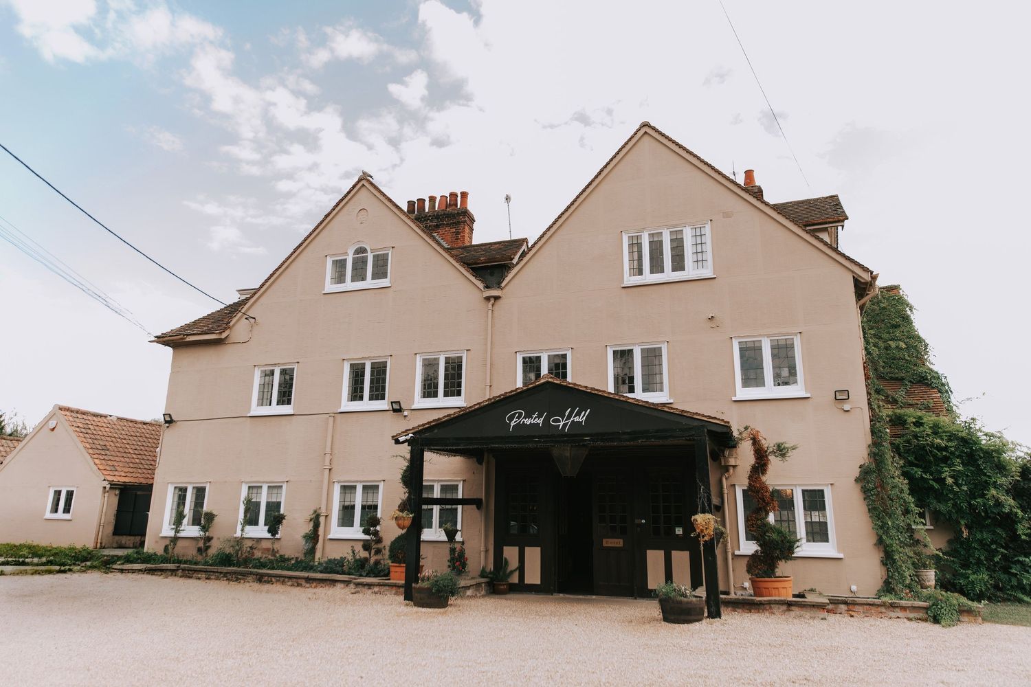 Prested Hall - charming English countryside hotel with a beige facade, black entrance canopy, and ivy-covered walls.