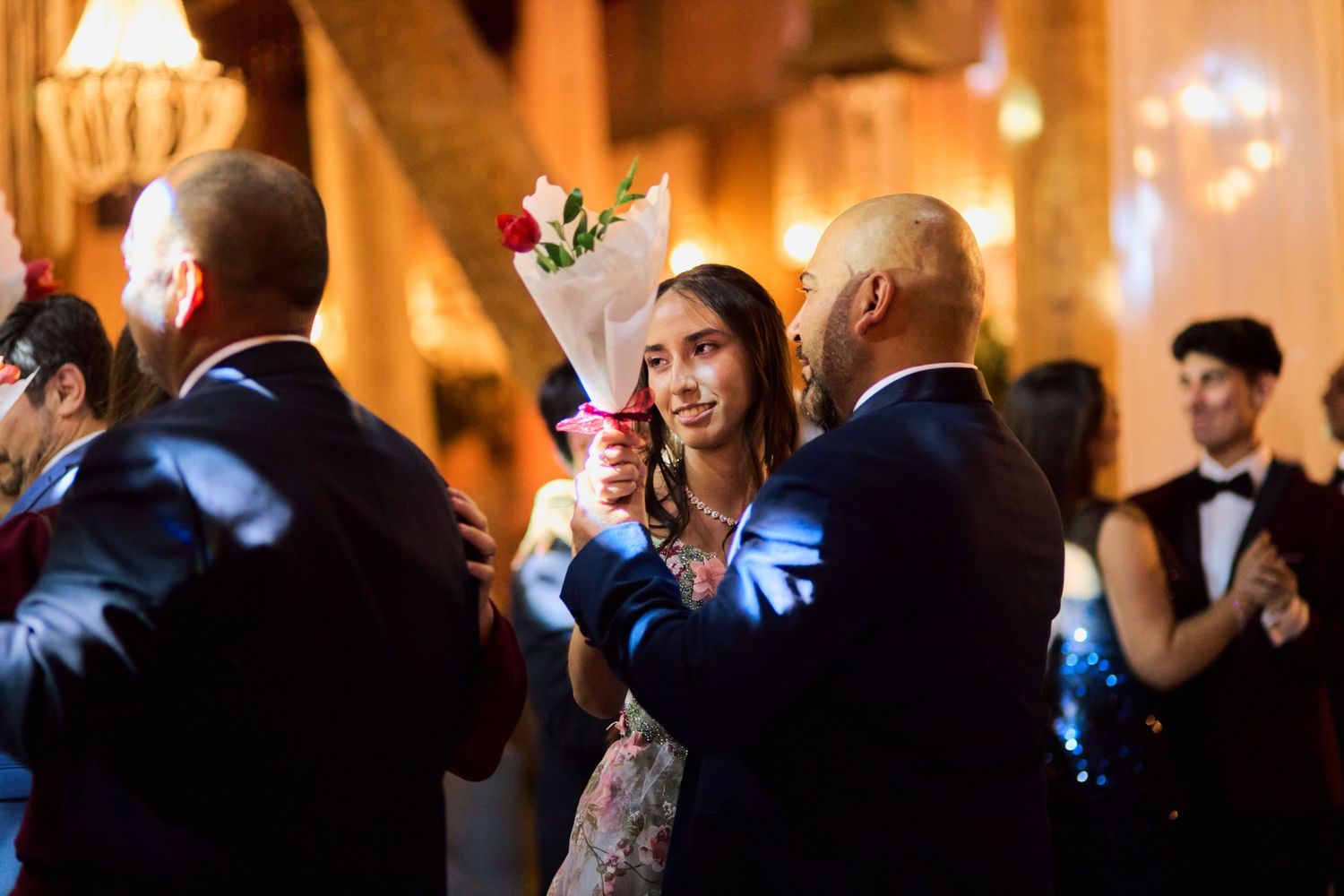 Wedding guests dance and celebrate on a dimly lit dance floor during an evening reception celebration.