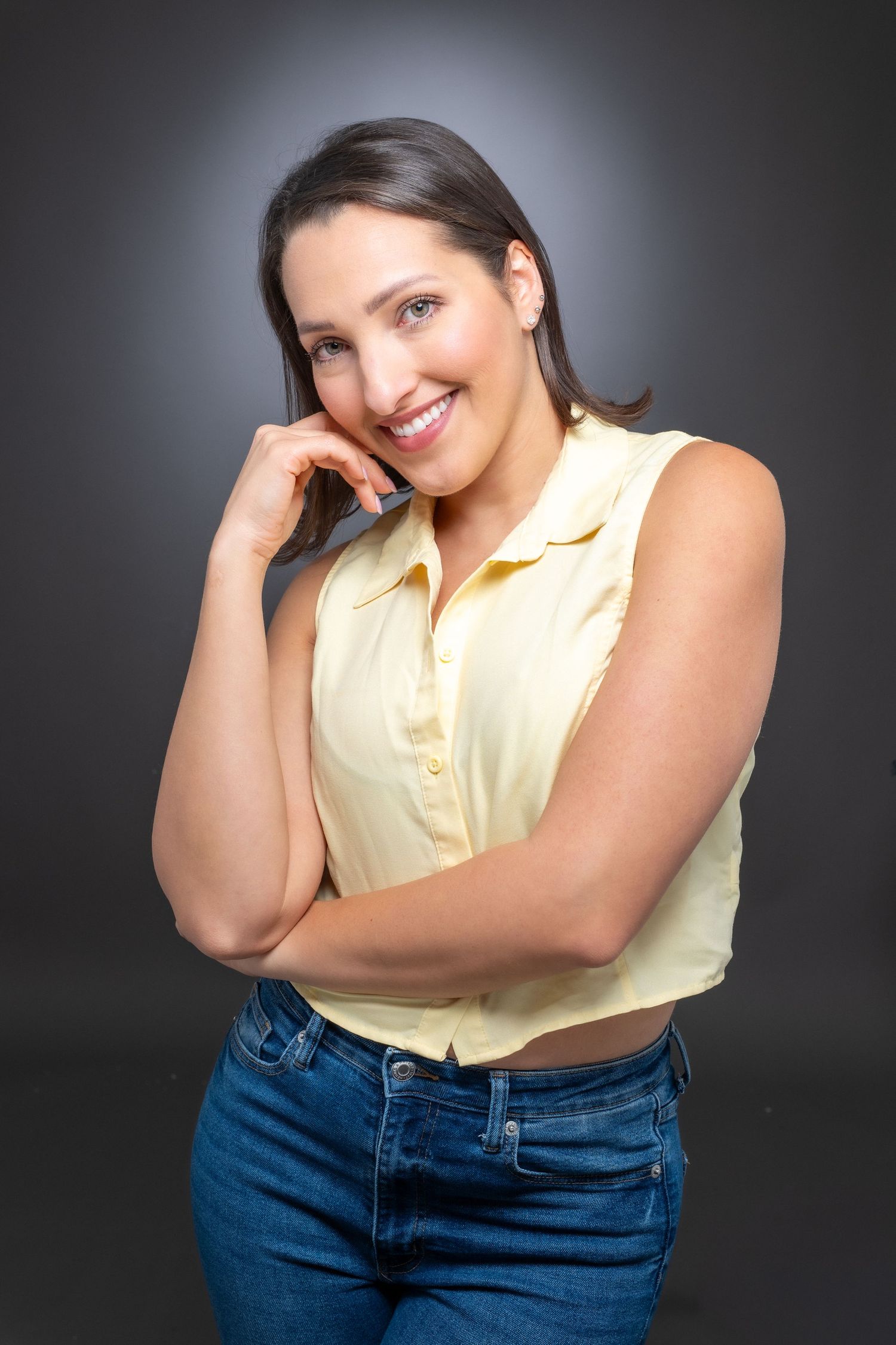 A person wearing a black long-sleeve turtleneck and blue jeans poses against a dark background in a studio setting.