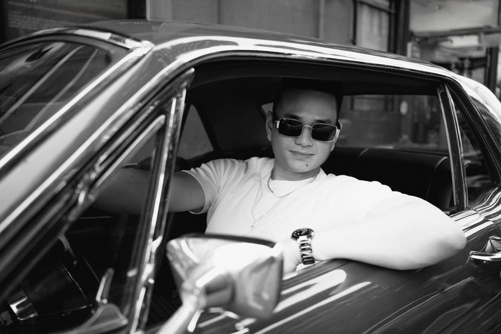 Stylish man wearing sunglasses sitting in driver seat of classic vintage car, black and white photo.