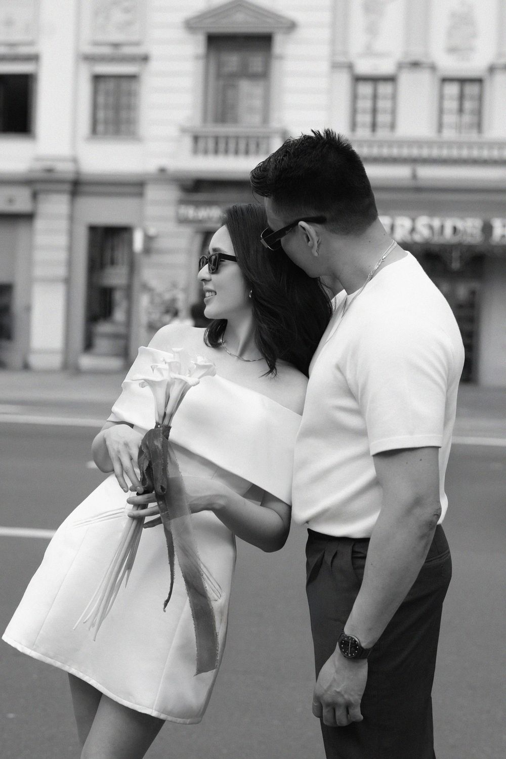 Black and white photo of a stylish couple sharing a romantic moment on a city street.