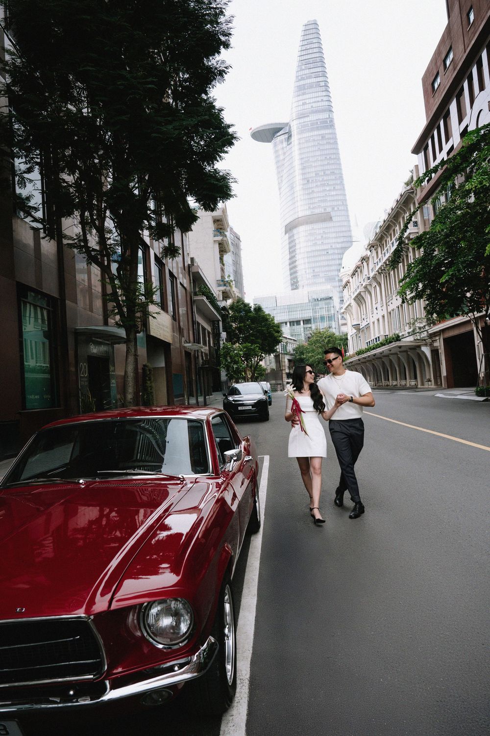 Couple walking past a red vintage Mustang on a city street.