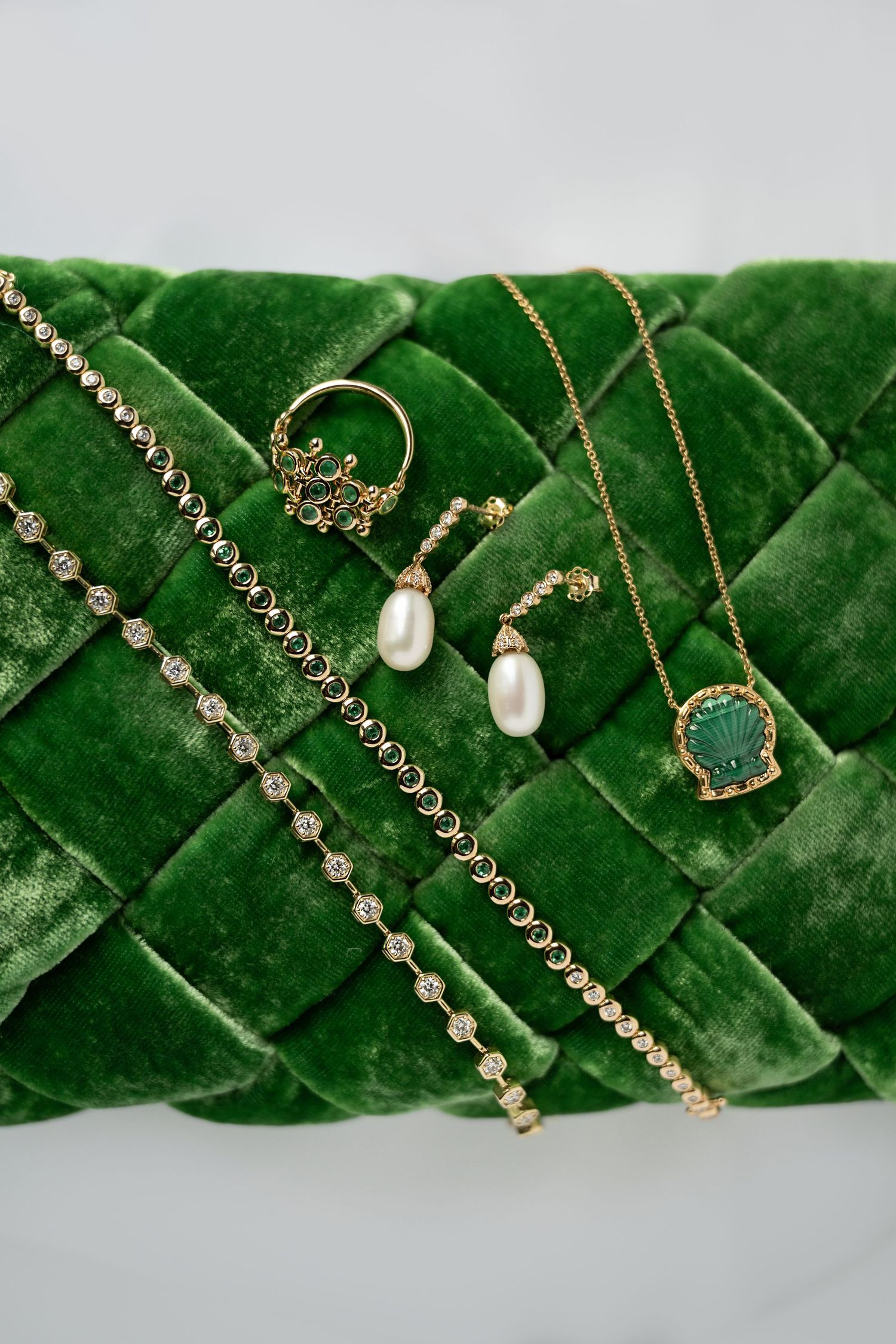 Gold jewelry set with pearl drop earrings, diamond bracelets, shell pendant necklace on green velvet display.