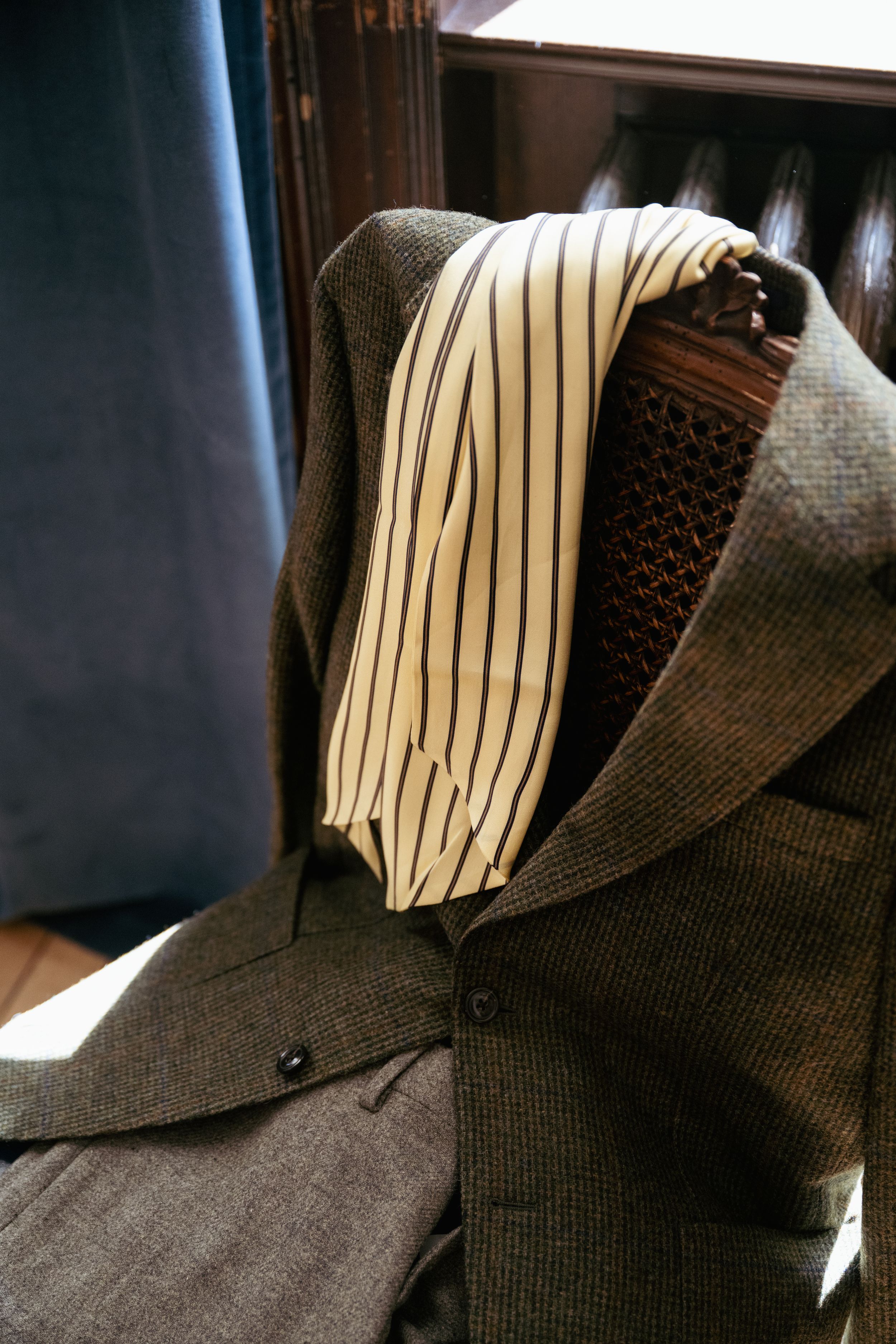 A tailored green tweed blazer displayed on a mannequin with a white striped dress shirt, showcasing classic menswear styling.