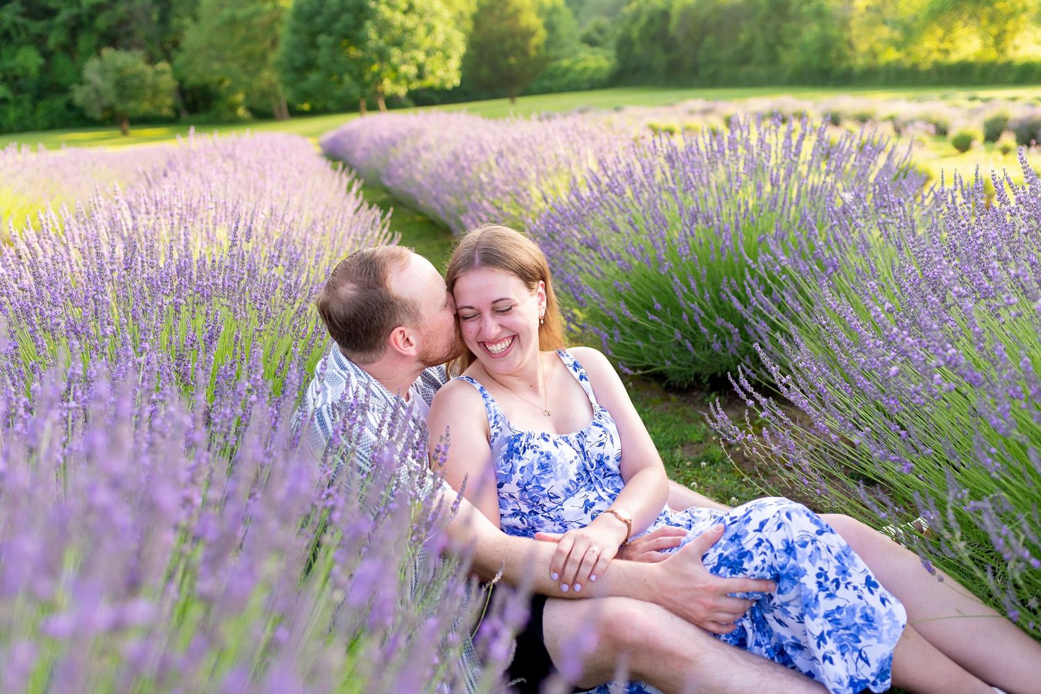 Couple relaxing in a blooming lavender field, woman in floral dress smiling joyfully on a sunny day.
