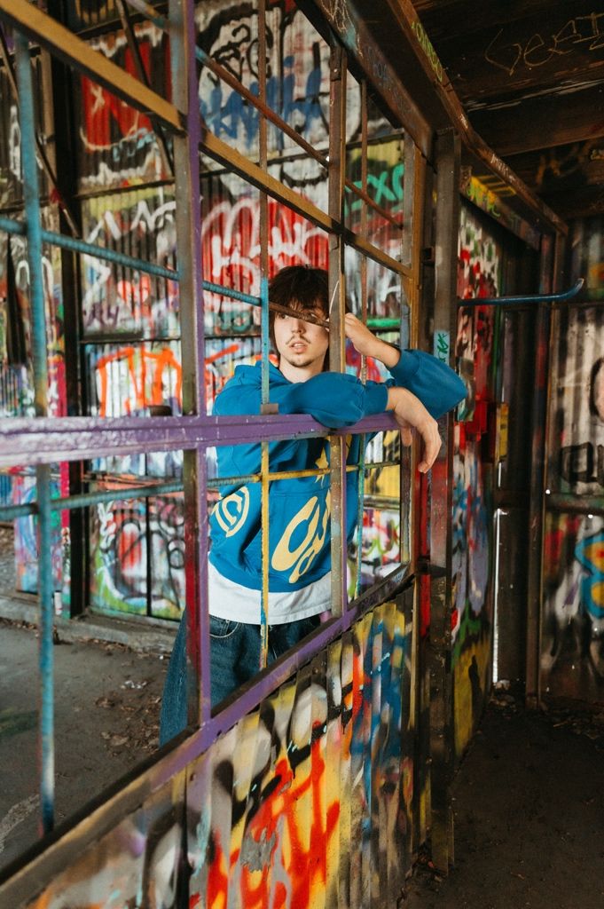 Teen boy leaning on colorful graffiti-covered metal bars in vibrant urban abandoned building setting.