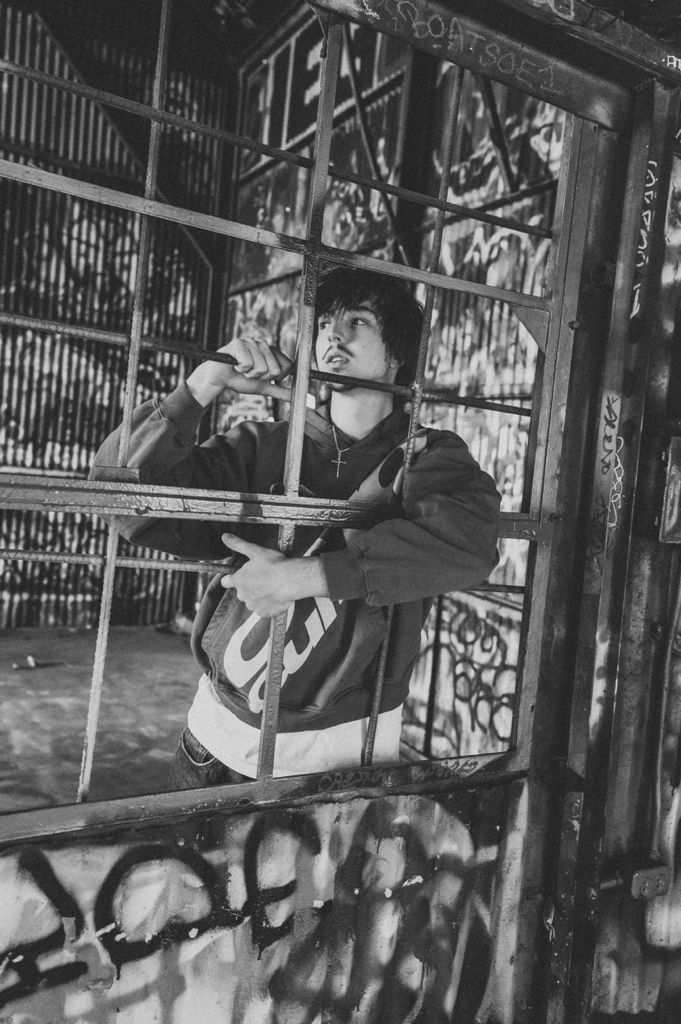 Young man gripping metal bars in abandoned graffiti-covered building, black and white urban photography.