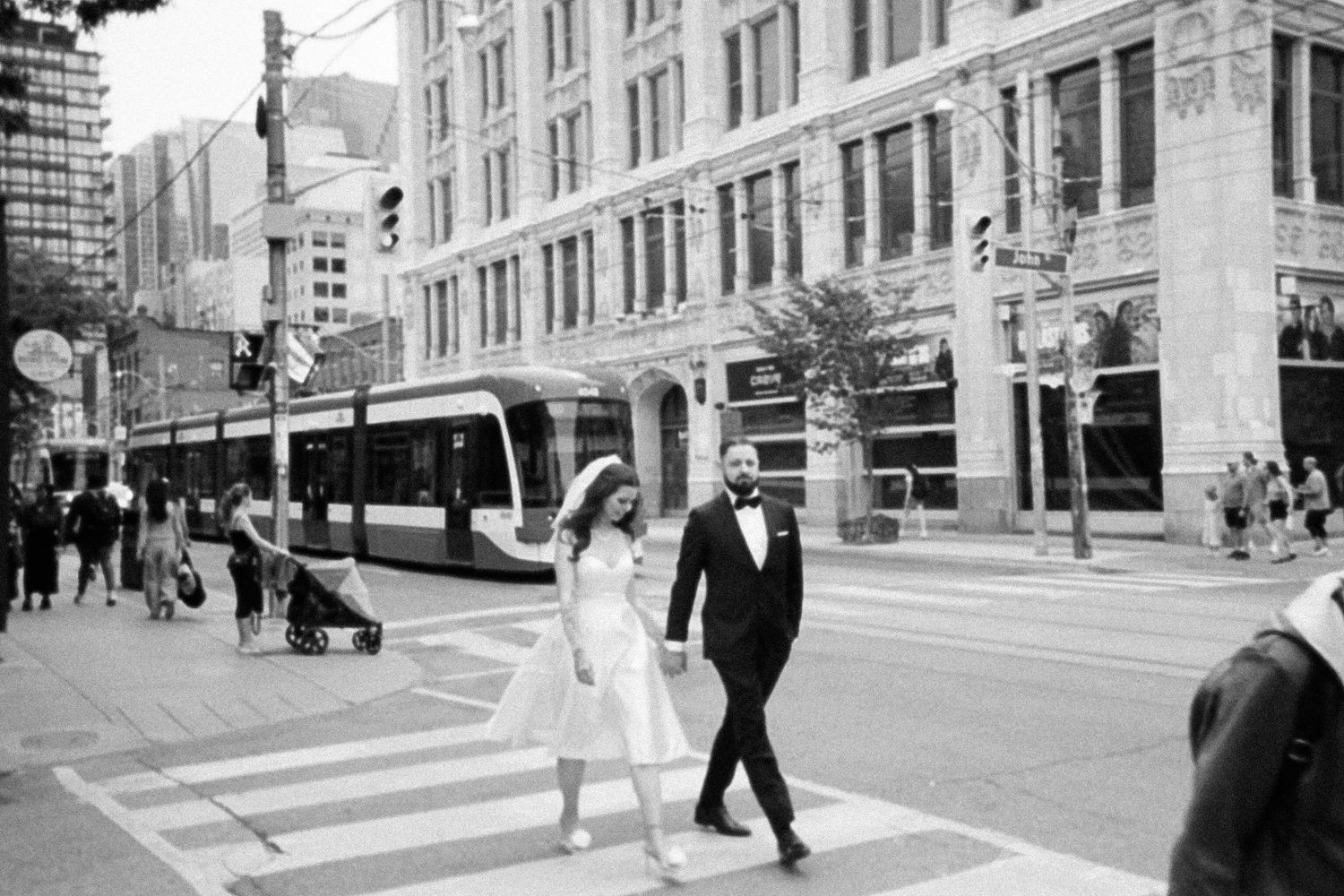 35mm film photo of bride and groom crossing the street in Toronto. Black and white.