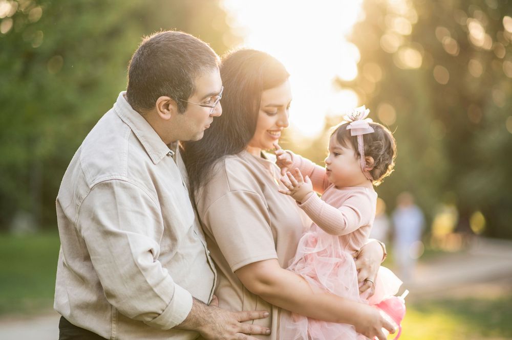 Loving family of three sharing a sweet moment at golden hour in a lush green park setting.