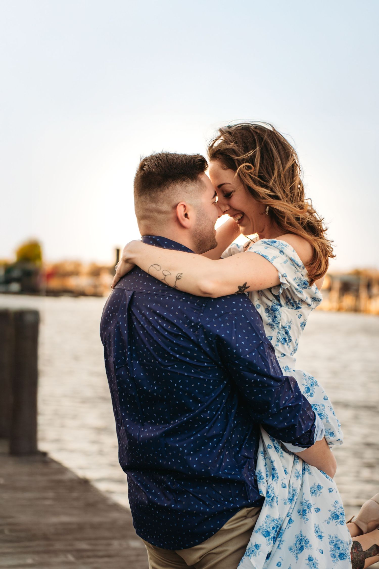 Delaware couple on a dock in Lewes, Delaware. Man is holding his fiancé in an close embrace with their faces close to each other
