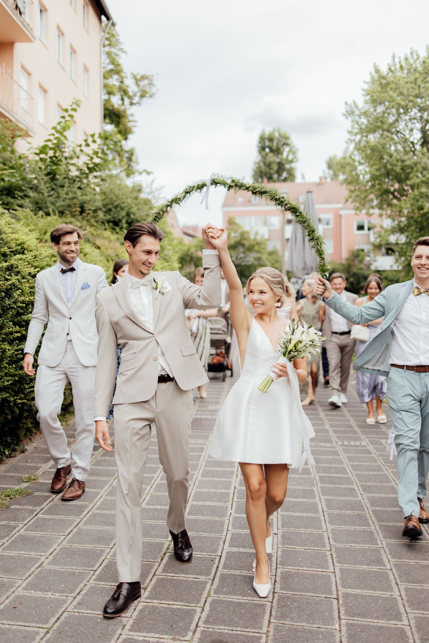 Bride and groom hold hands in the air smiling as their family and friends follow them to celebrate their wedding