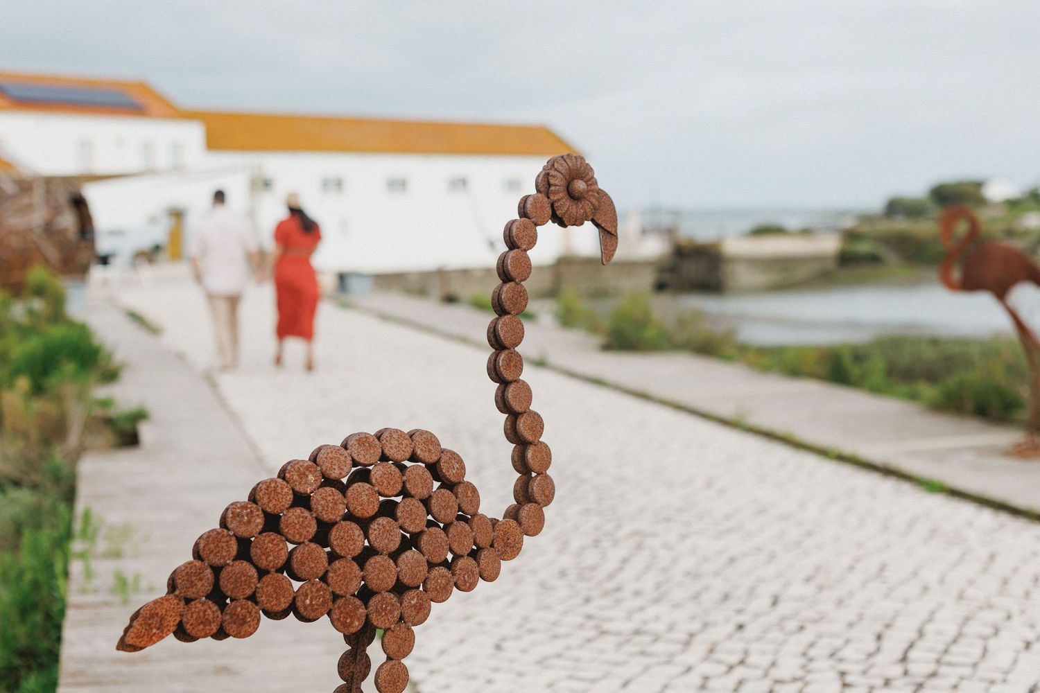 Creative detail shot of metal flamingo sculpture with couple walking in background at Moinho da Mourisca Setúbal