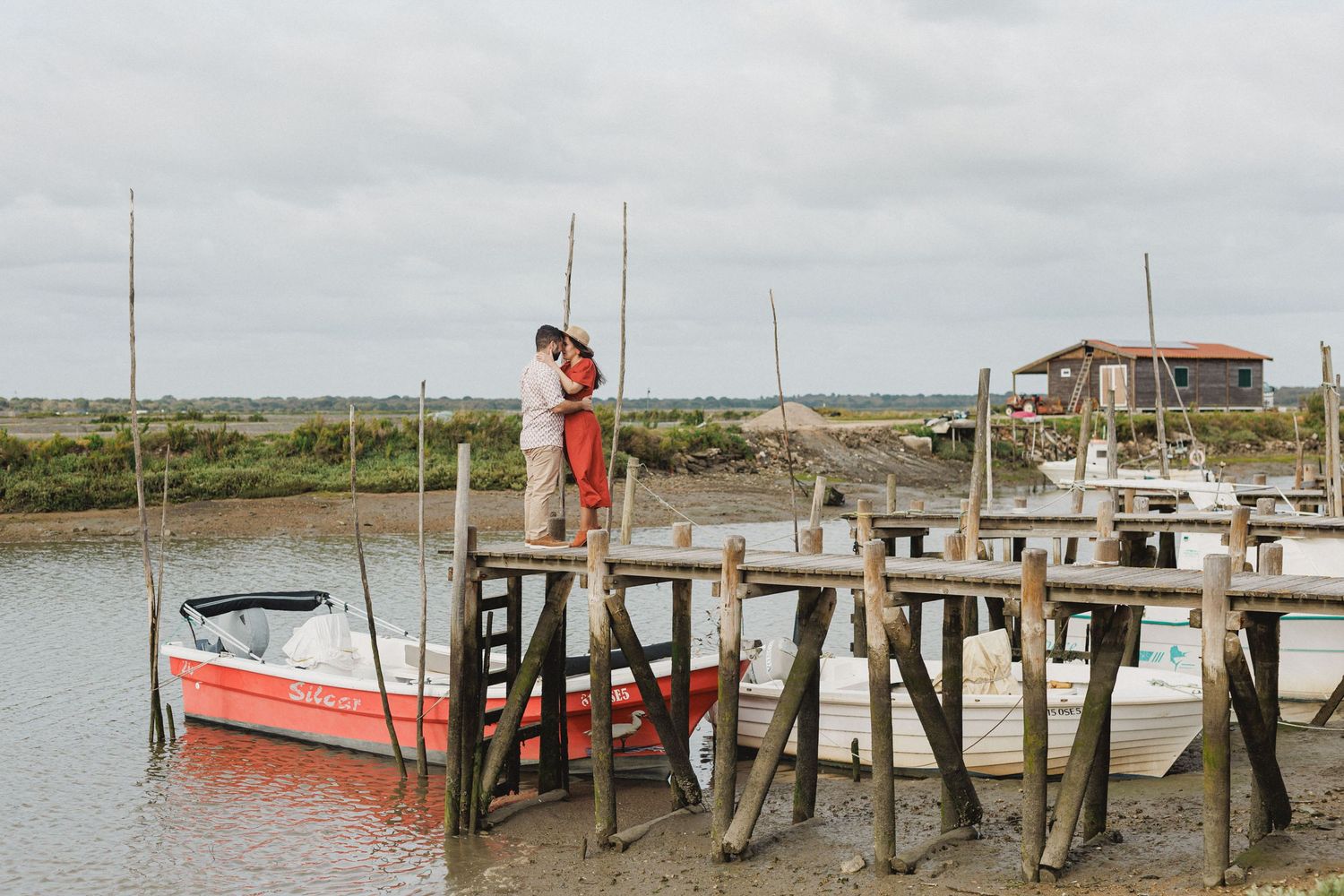 Engaged couple kissing on wooden pier with boats during pre wedding photoshoot in Setúbal Portugal